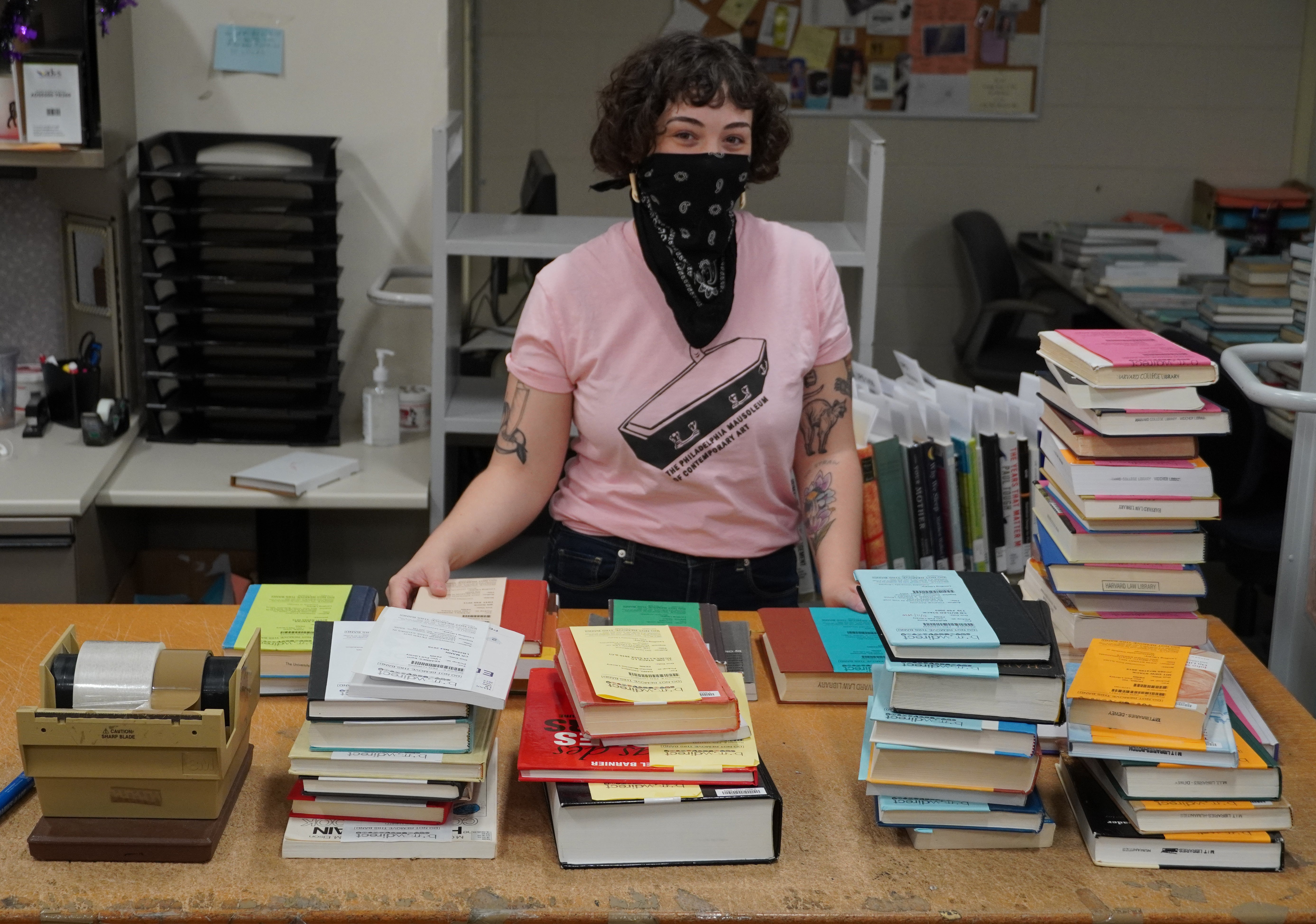 A librarian wearing mask is arranging books on a table.