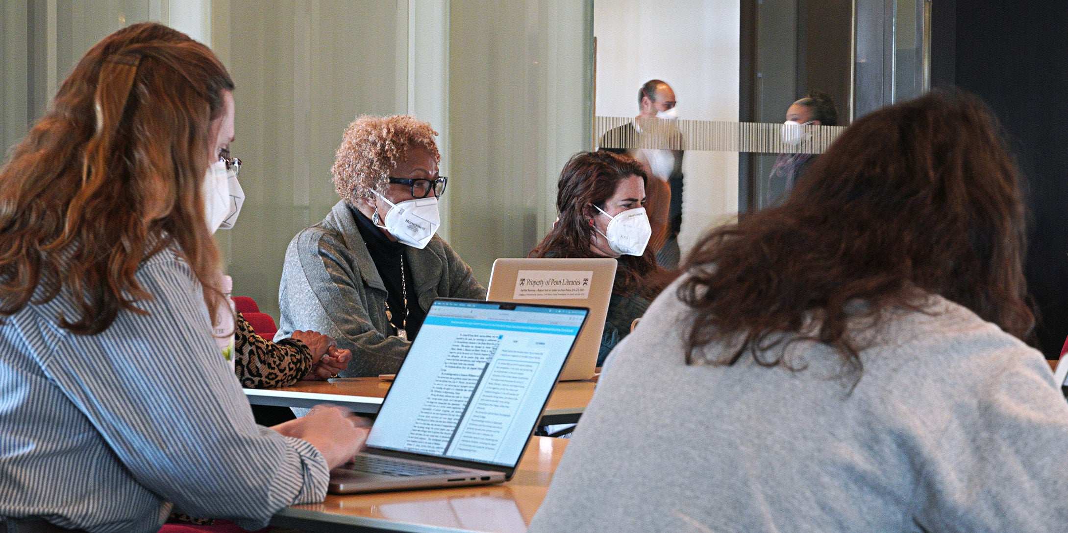 People in masks sitting around table with laptops