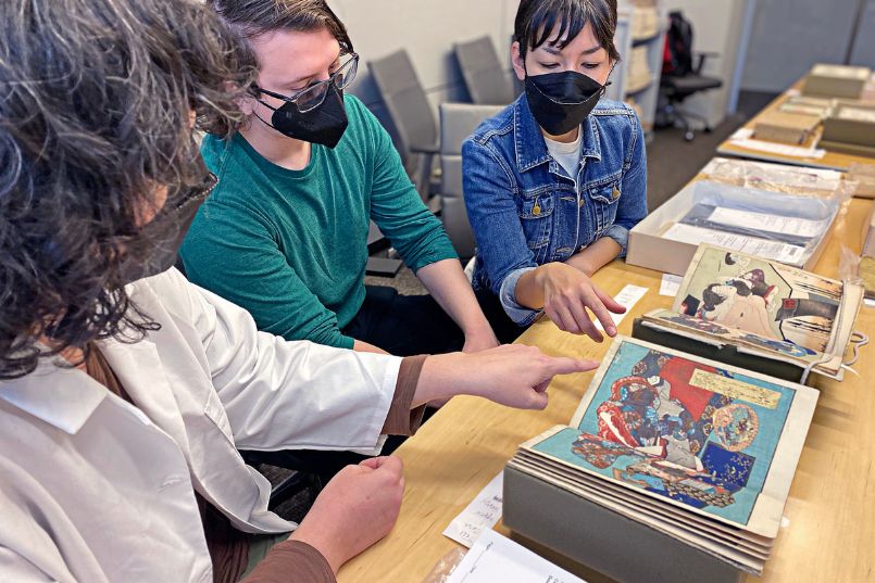 Tress exhibition curators look over several Japanese illustrated books