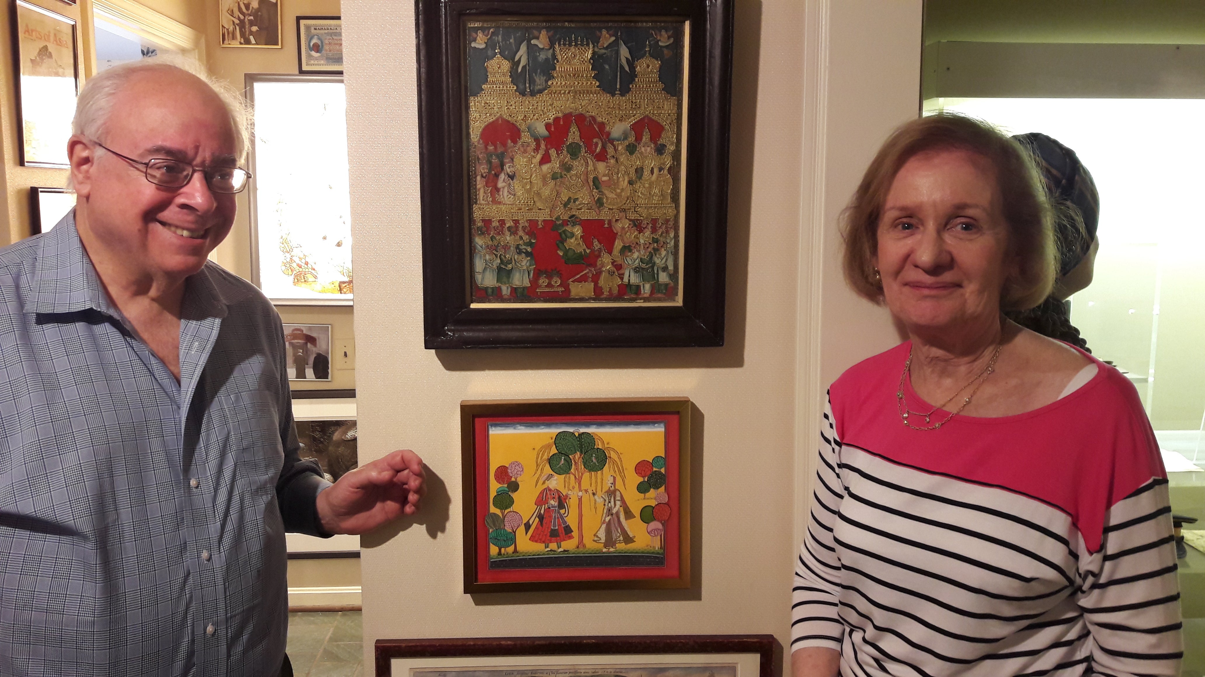Two individuals standing next to framed artworks.