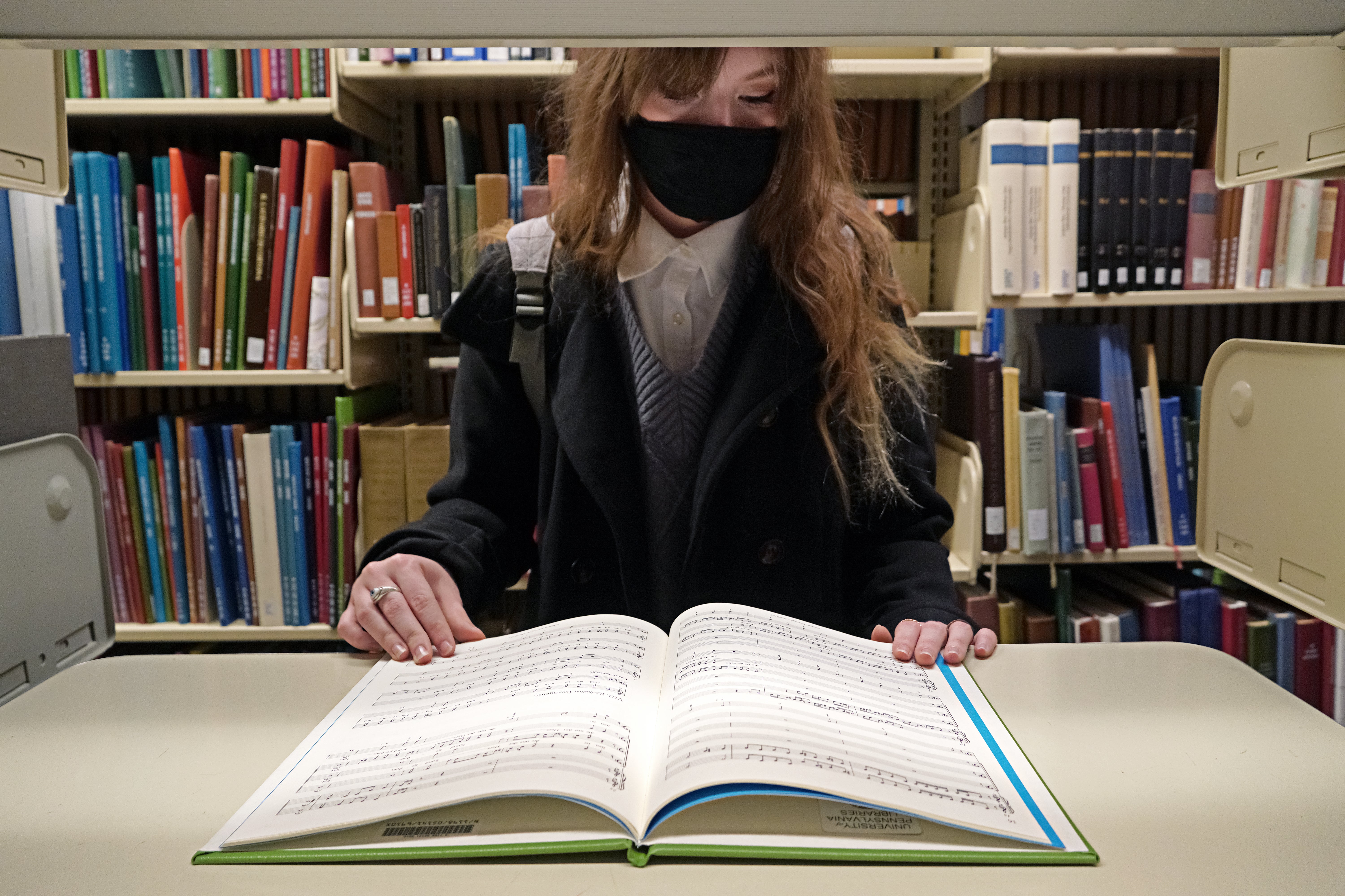A student looking down at a large open book on a bookshelf in Van Pelt Library.