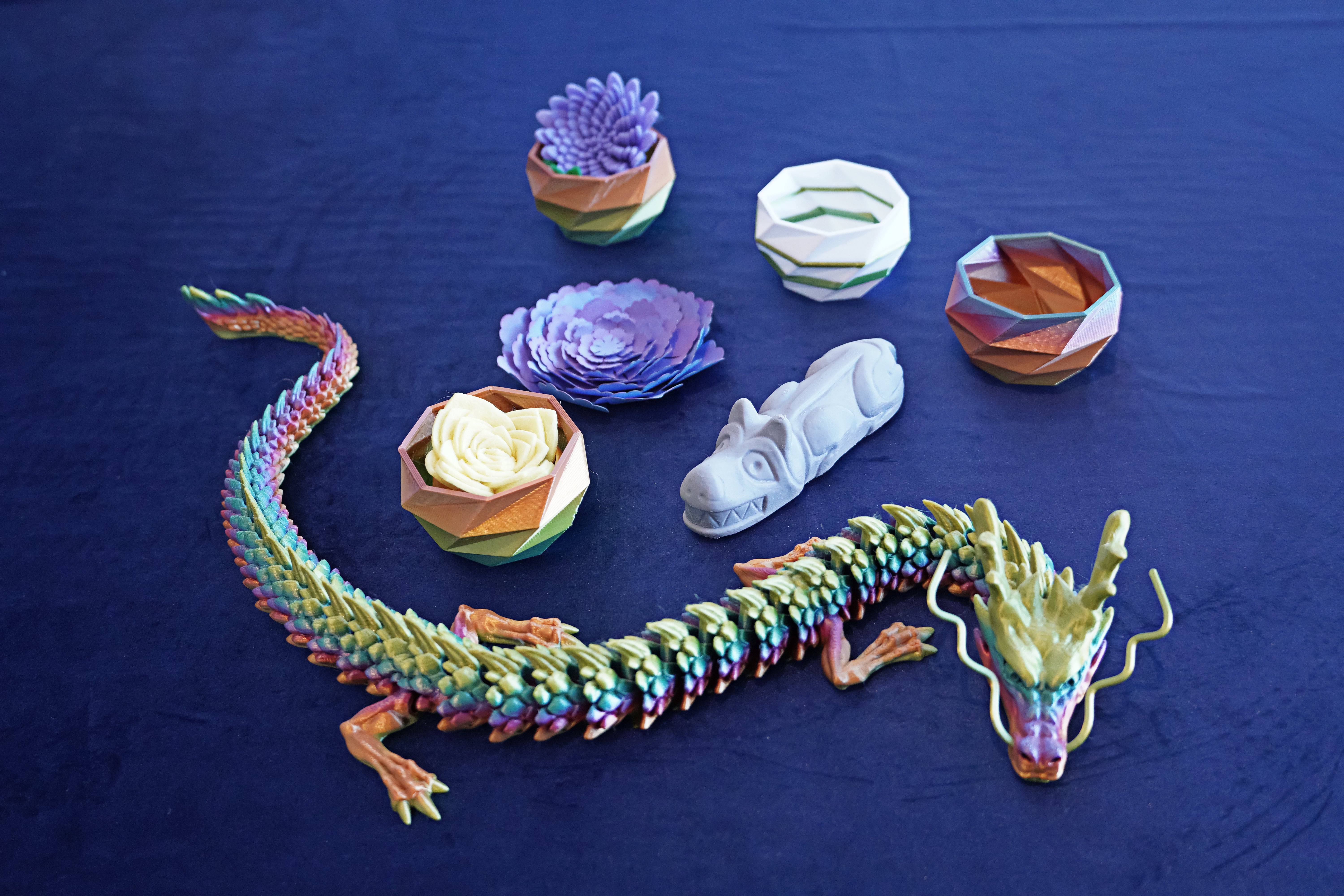 An assortment of 3-D printed toys are displayed, including a colorful dragon and some succulents.