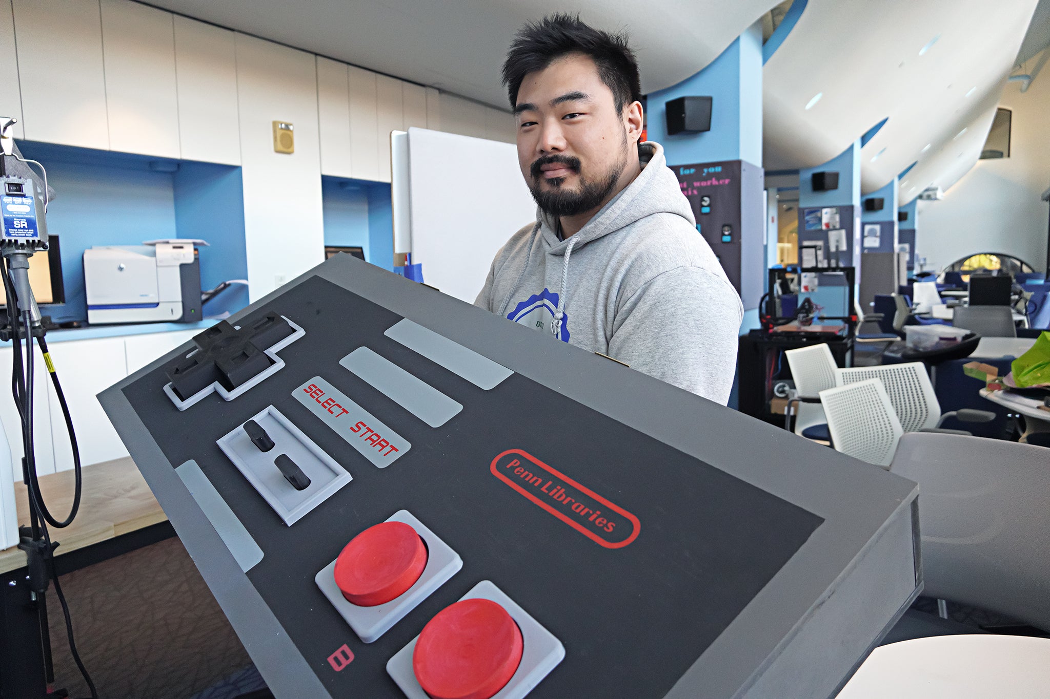 A person standing in the Education Commons makerspace holds a humorously larger-than-life model of a game controller.
