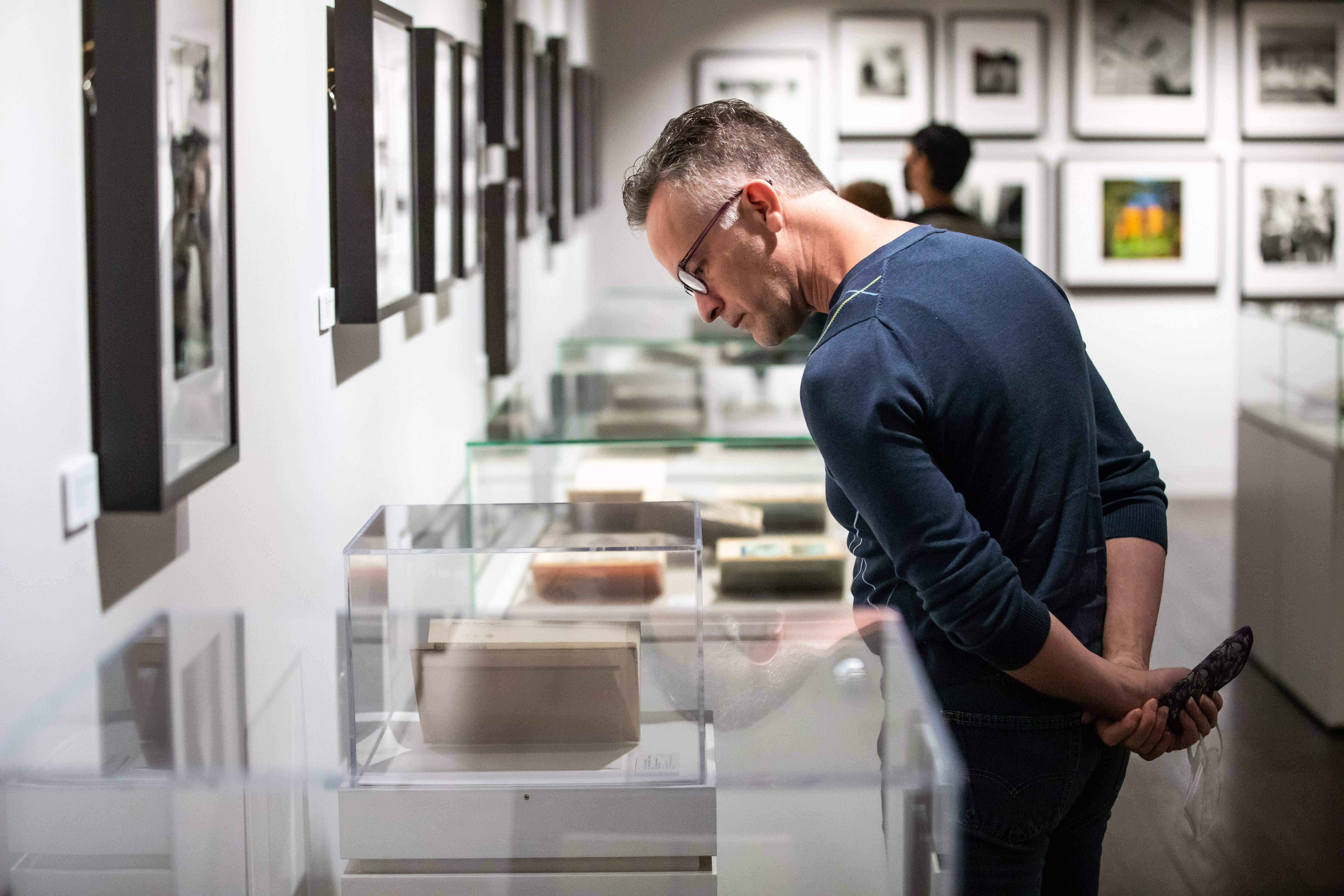 An individual looks down at a glass display case in an exhibit space with framed photos on the walls