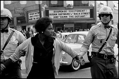 A Black woman's arms are restrained by two police officers