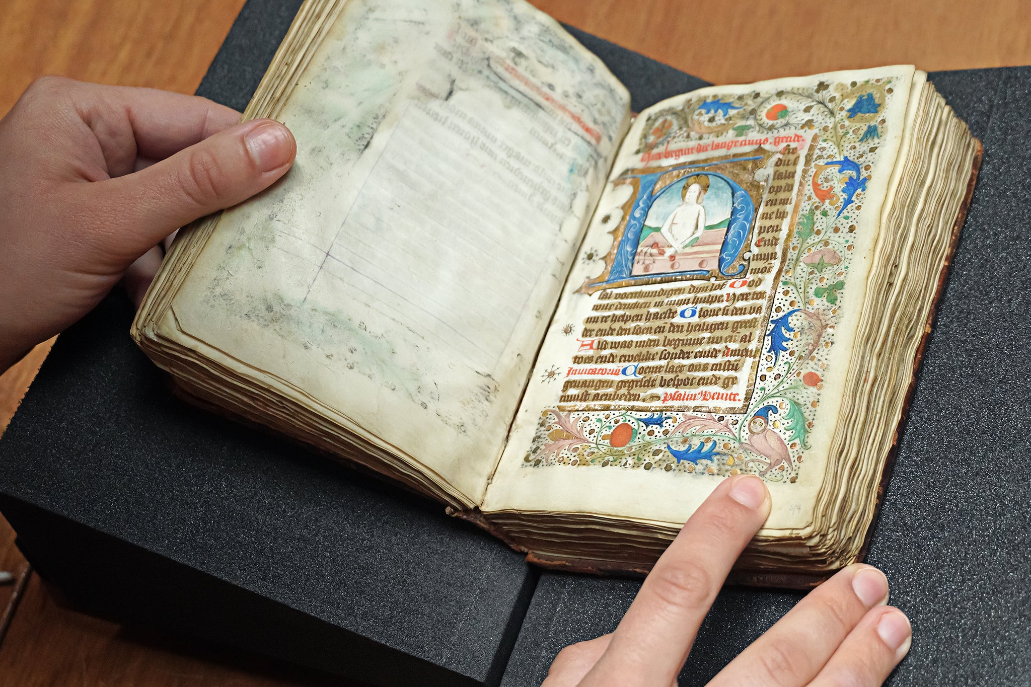 Looking down at an illuminated manuscript with hands holding it open.