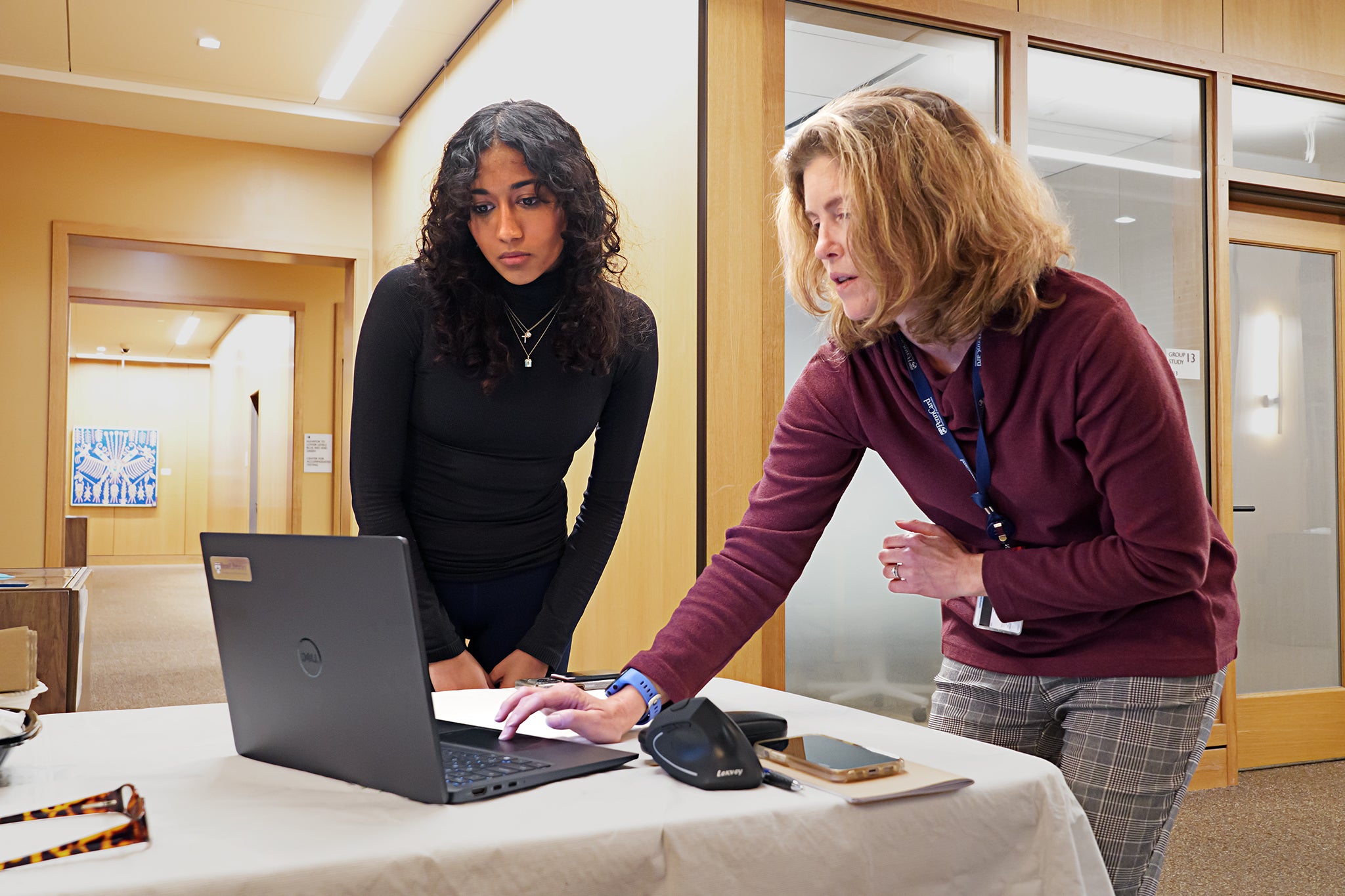 Two individuals are working together on a laptop in an office environment.