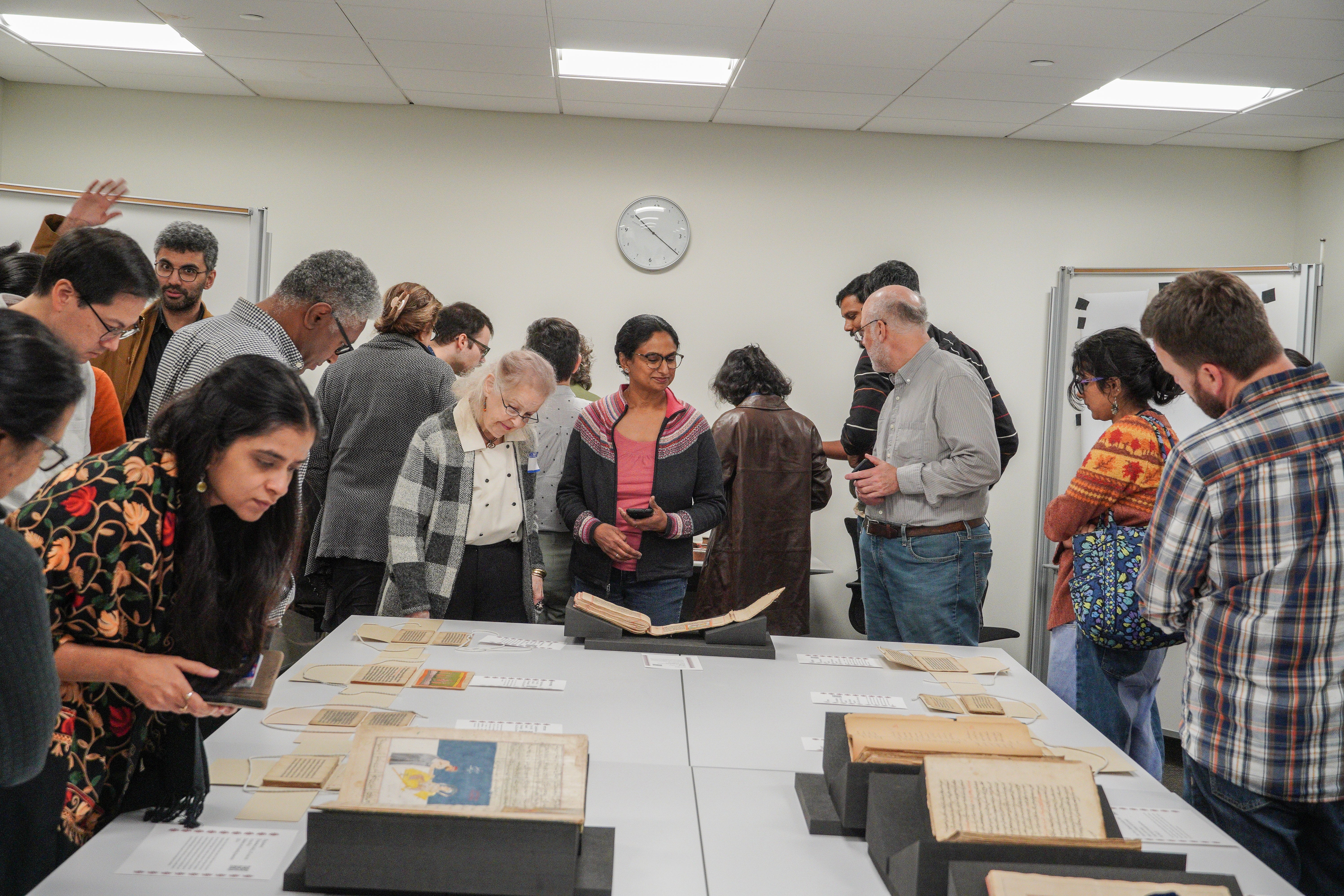 20 people gathered around a table looking at colorful manuscripts
