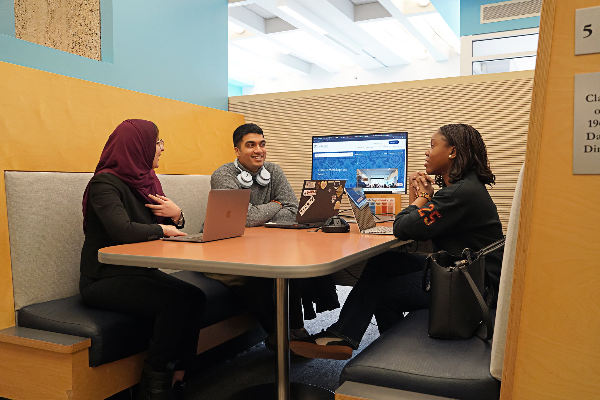 3 students sitting in a study booth, enthusiastically talking.