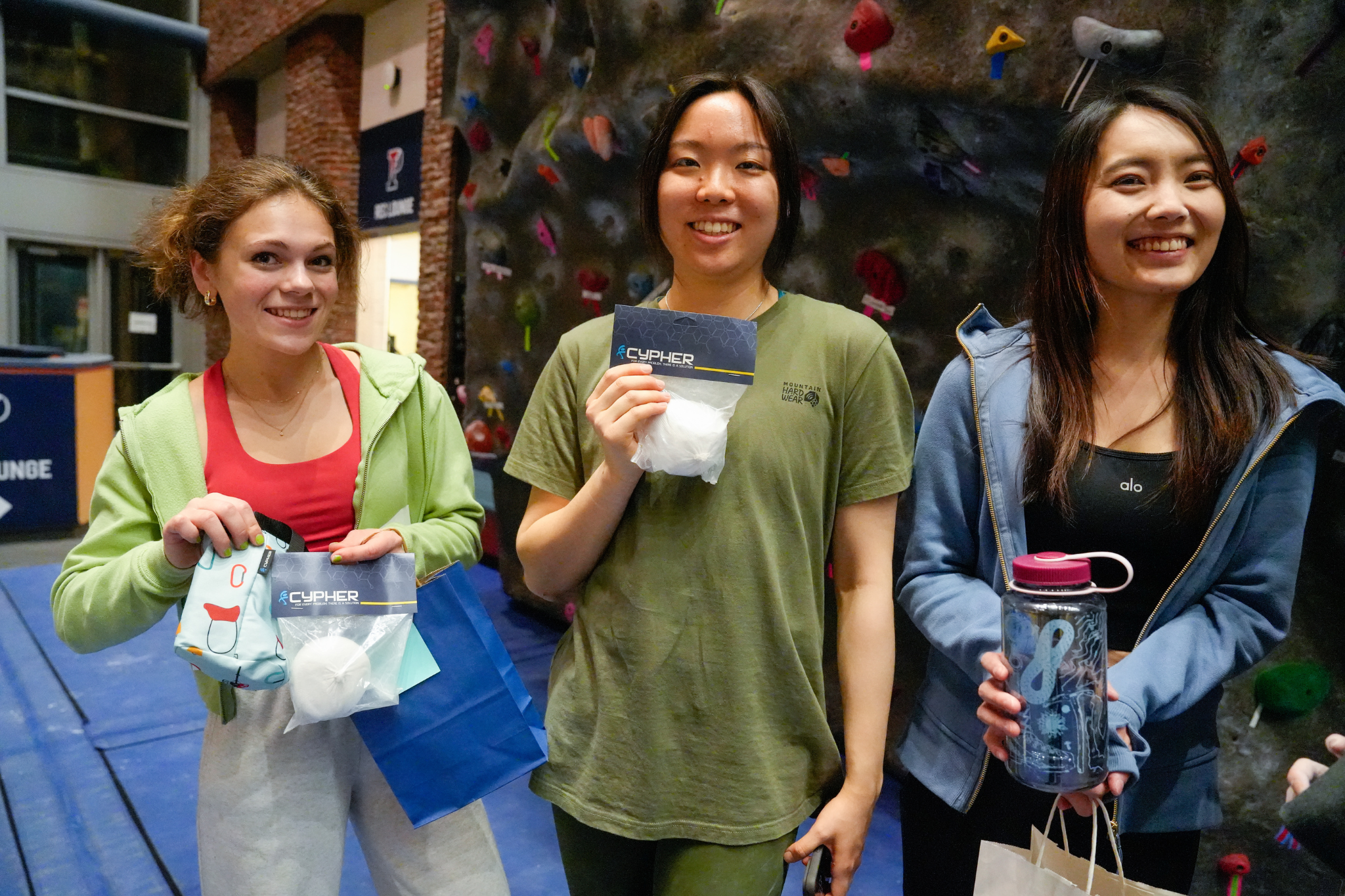 3 female Penn students in front of the climbing wall