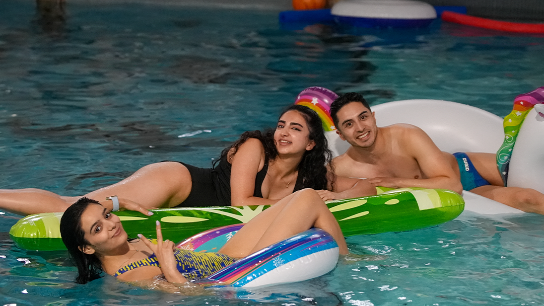 Group photo of 3 swimmers floating on pool toys at Penn