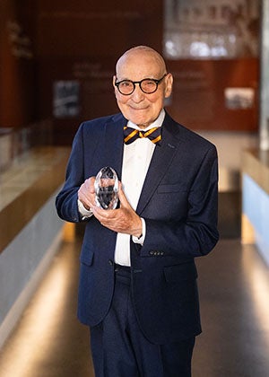 Person in suit holding crystal award and smiling at camera