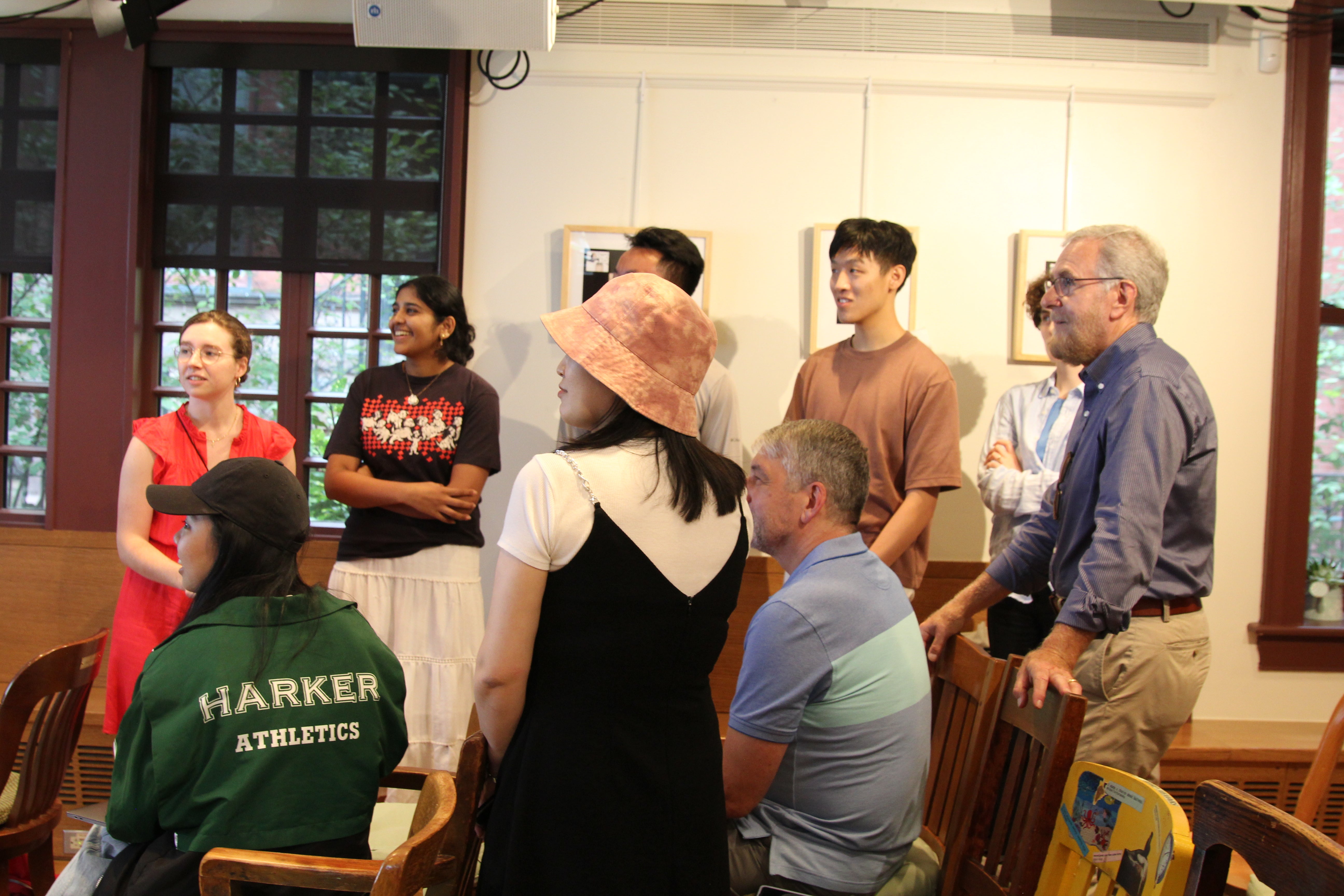 Workshop participants standing and seated in a room with framed artwork on the walls, all looking toward the front with amused expressions