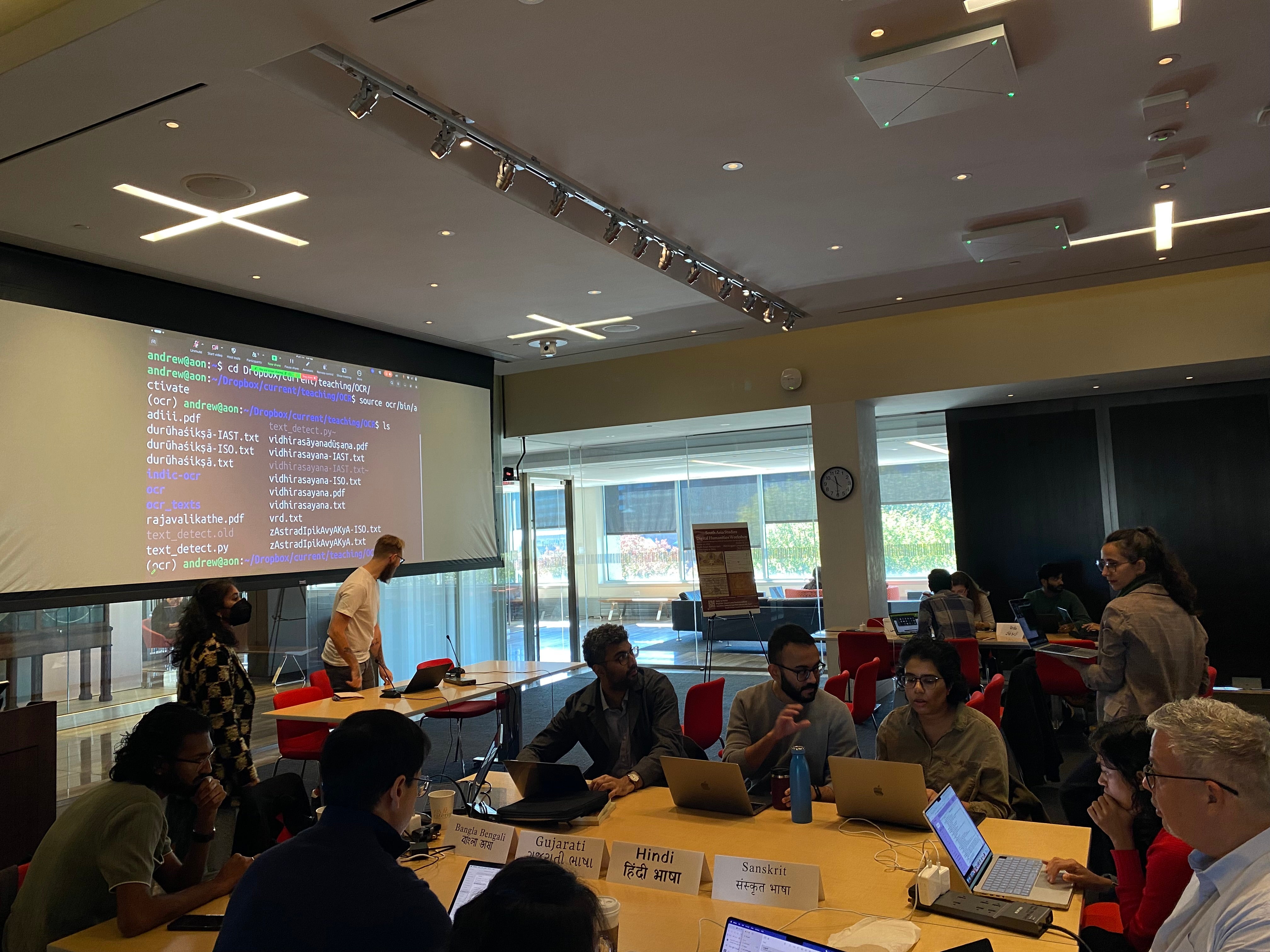 people at many tables with laptops looking at large projection of command line screen in a large room