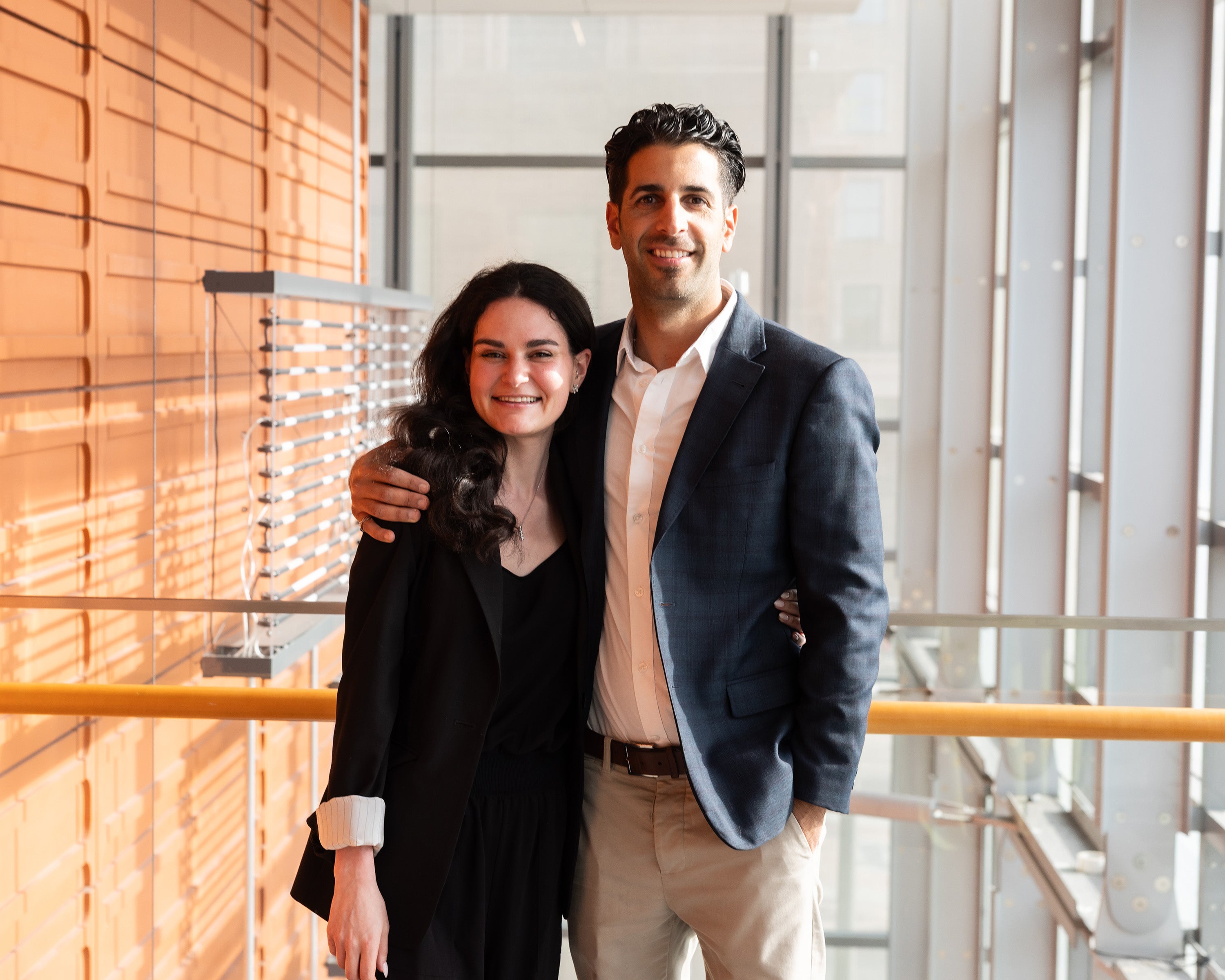 Two people stand facing the camera, smiling with their arms around each other