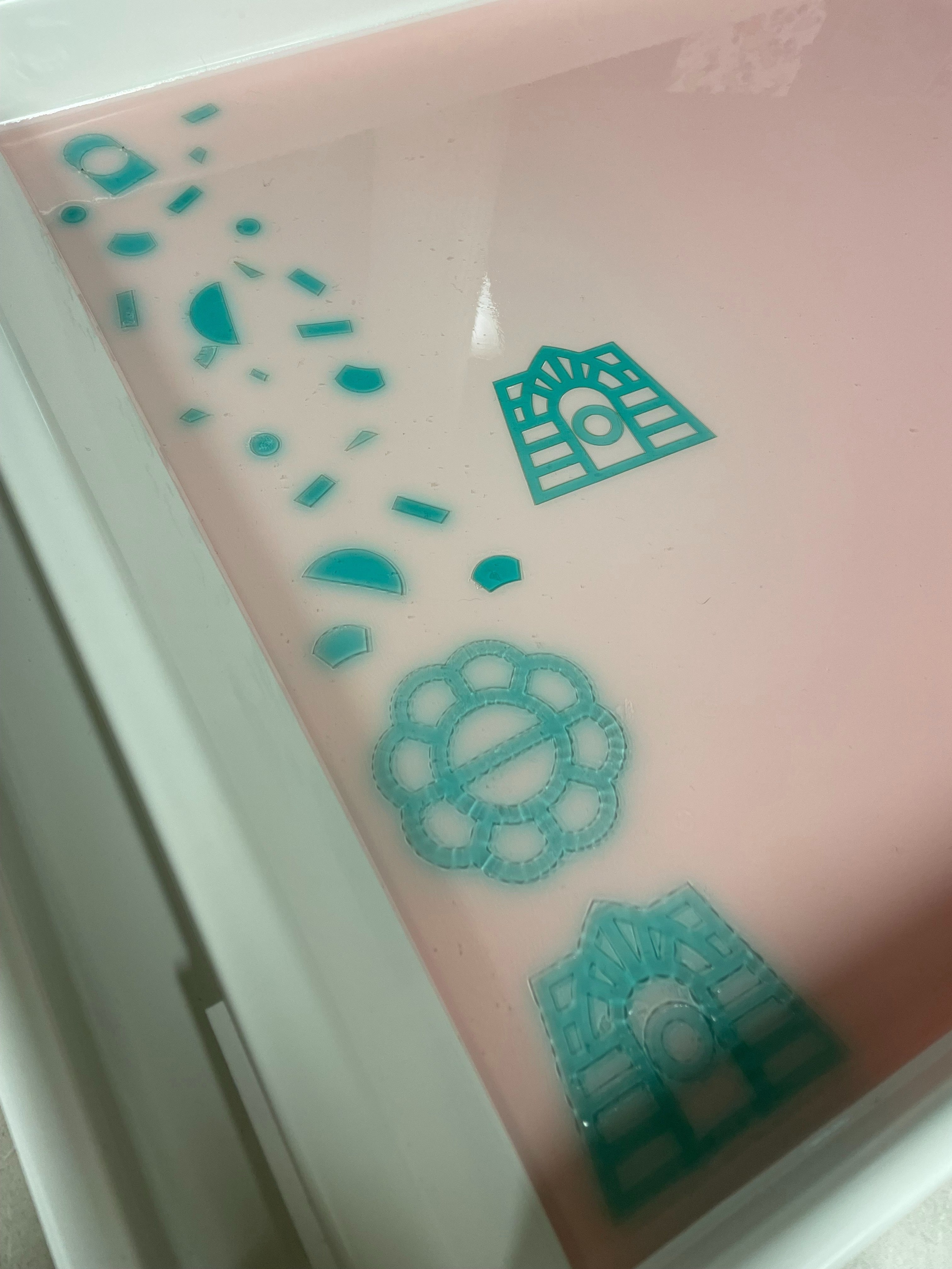  Light pink liquid in a white tray with various teal, geometric, and floral shapes floating and submerged.