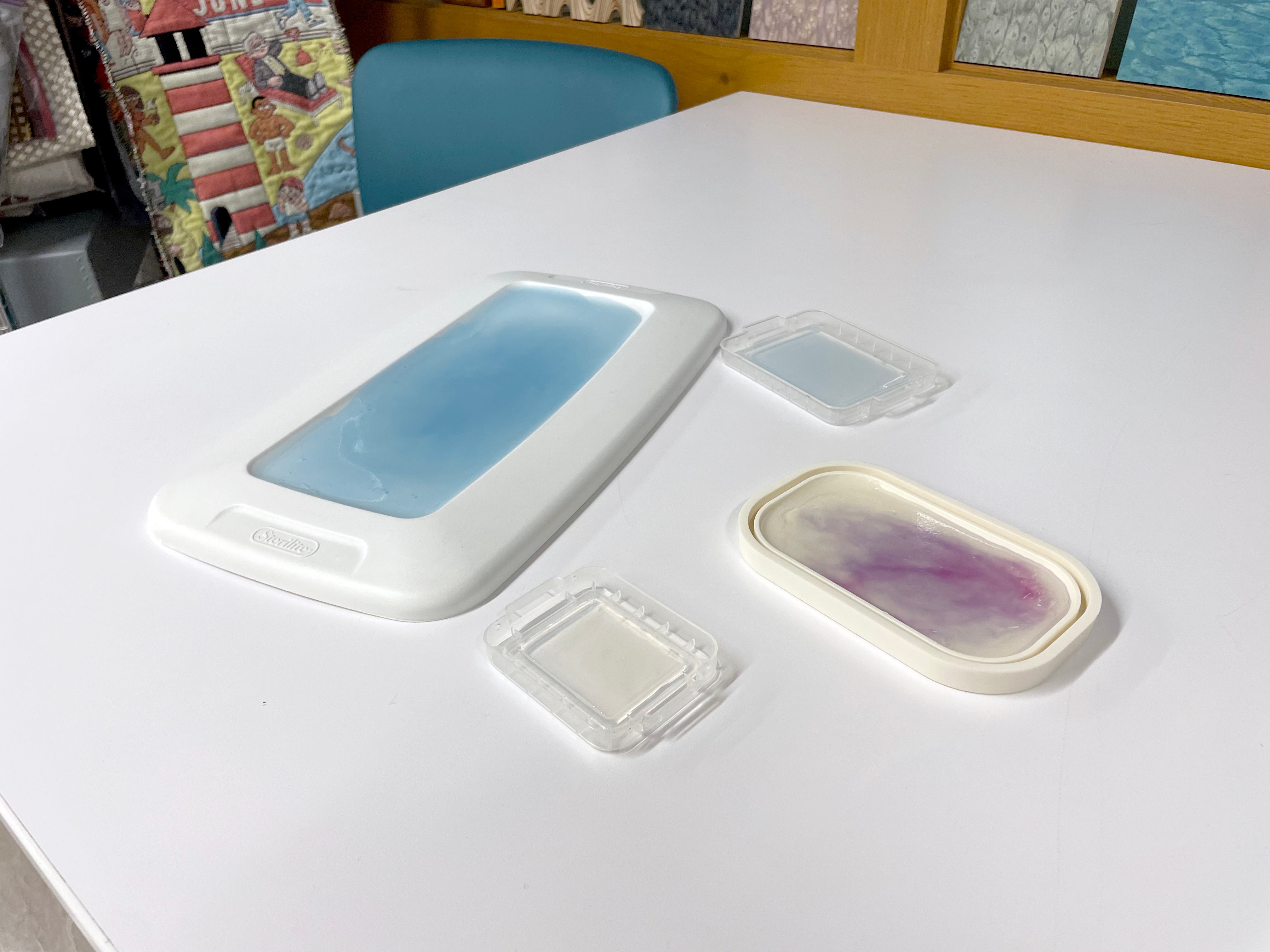 Four container lids of various sizes sit on a white table. The lids are white with various colors in the center.