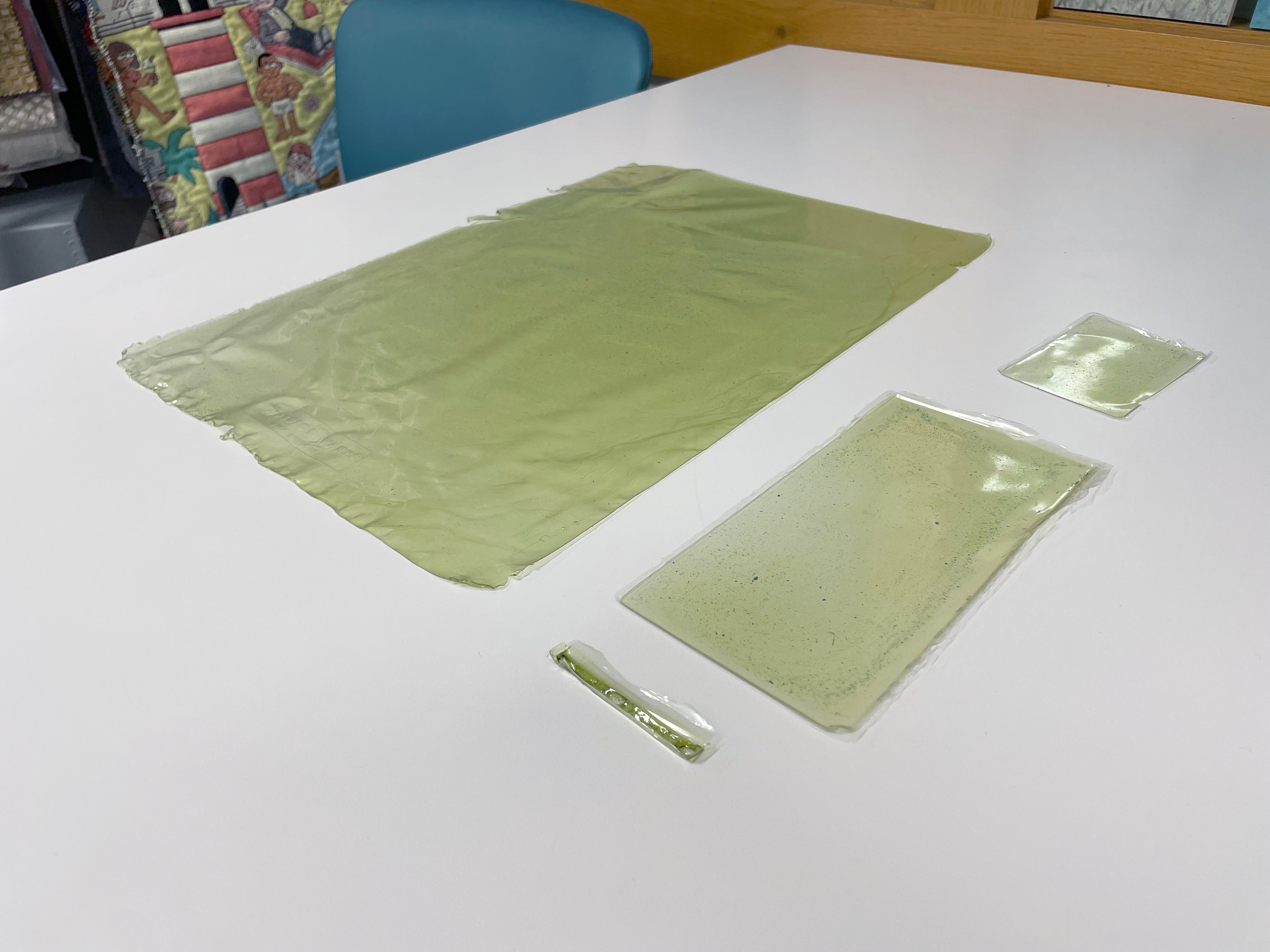 Sheets of what appear to be plastic in various sizes and shades of light green are arranged on a white table.