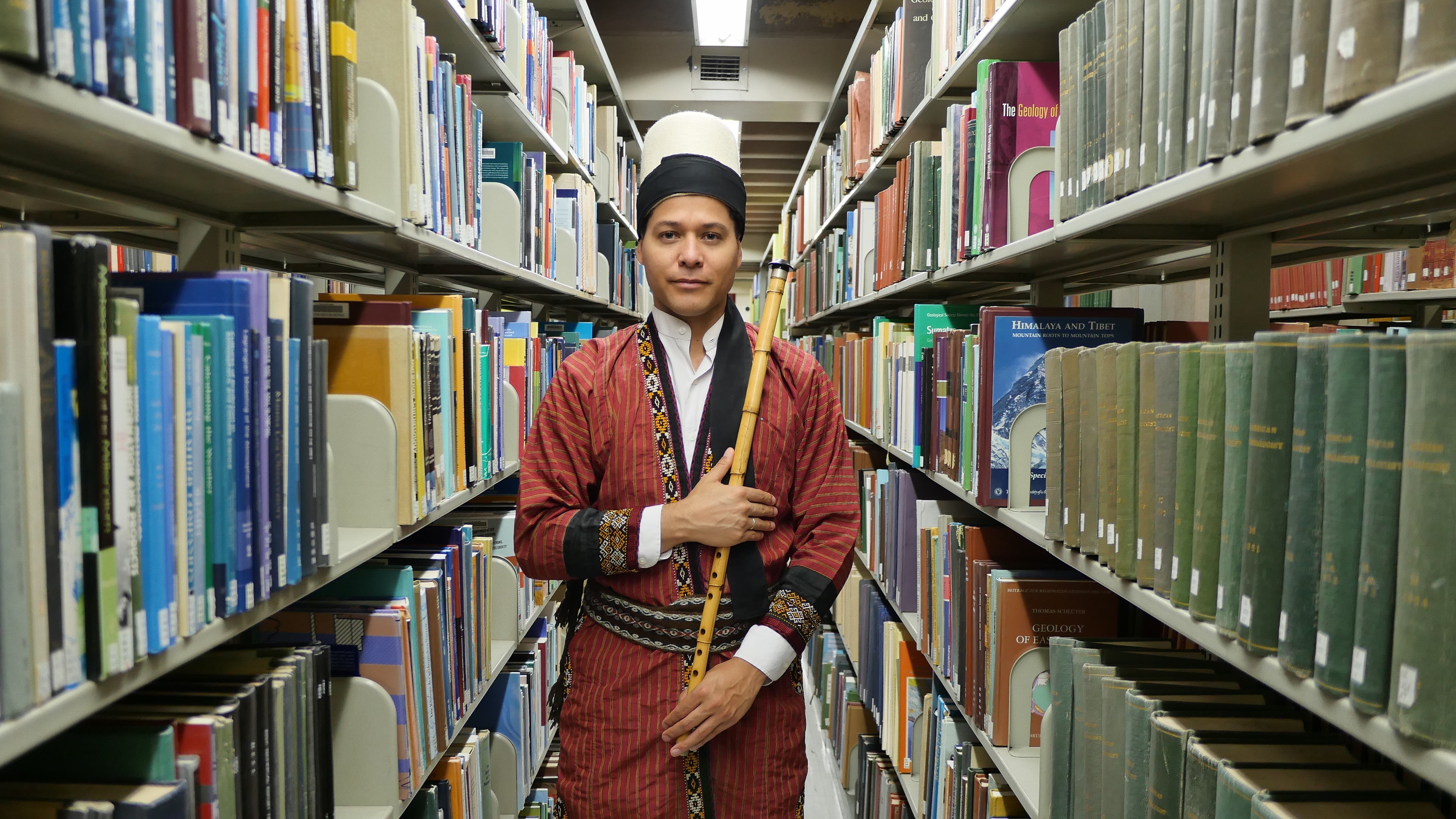 Juan Castrillón holding a ney flute in the library stacks.