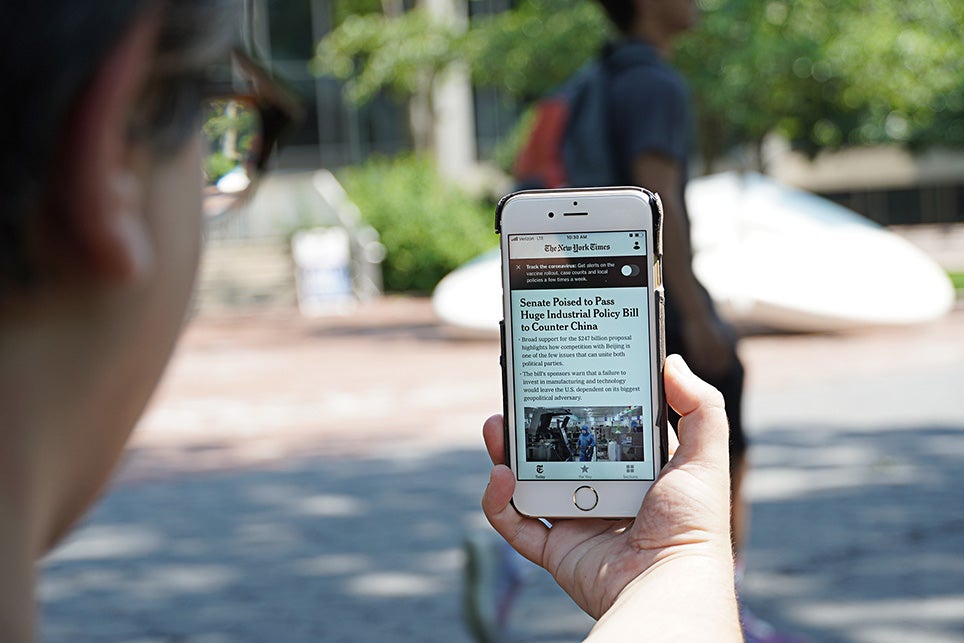Individual holding mobile phone on Penn's campus with New York Times app visible on screen