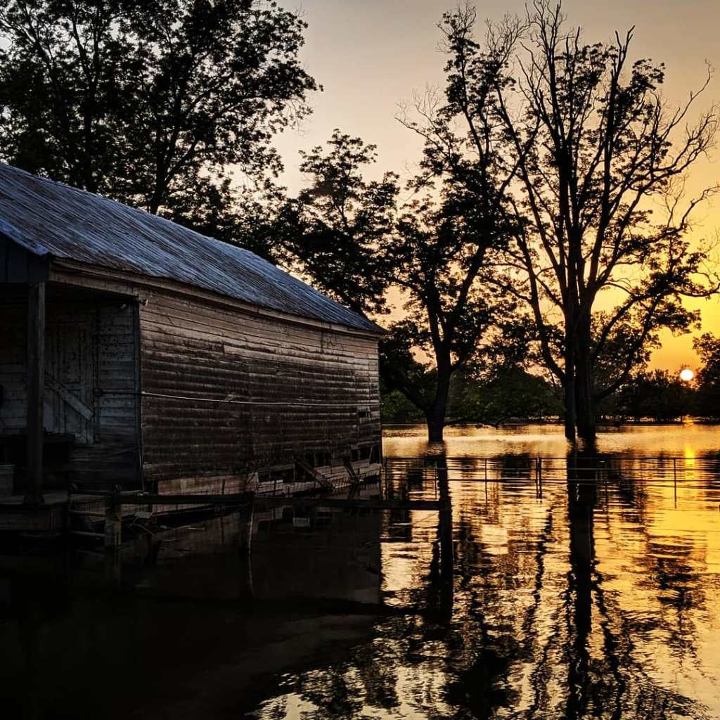 Sunset behind a house reflected on water.