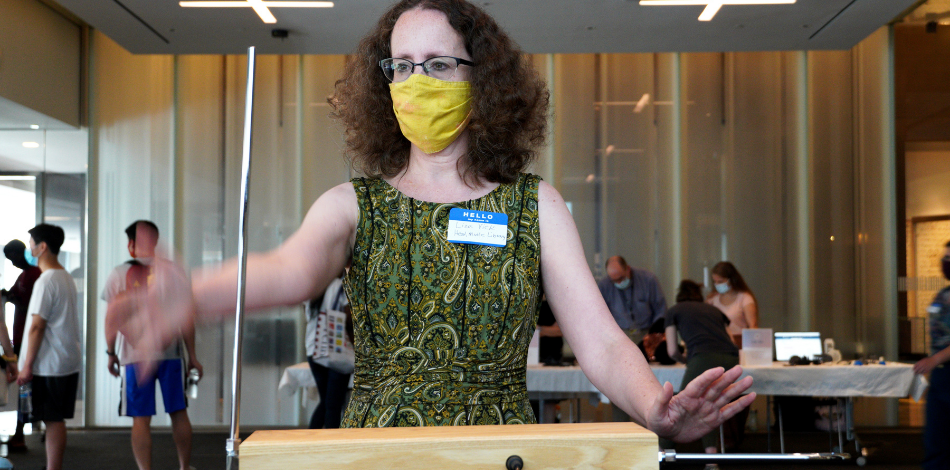 A woman wearing a face mask stands with her hands stretched out in front of her, playing the theremin.