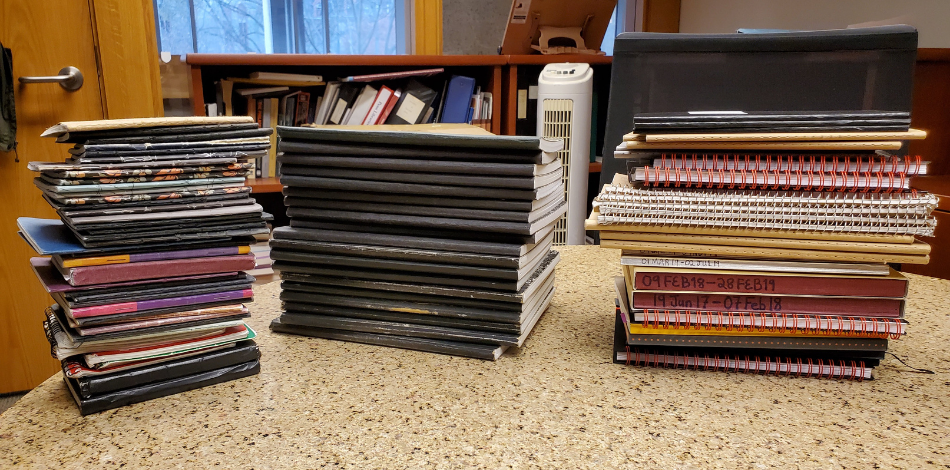 Three large stacks of bound notebooks sitting on a formica table.